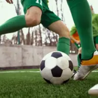 soccer ball in a football pitch and 2 guys in green playing